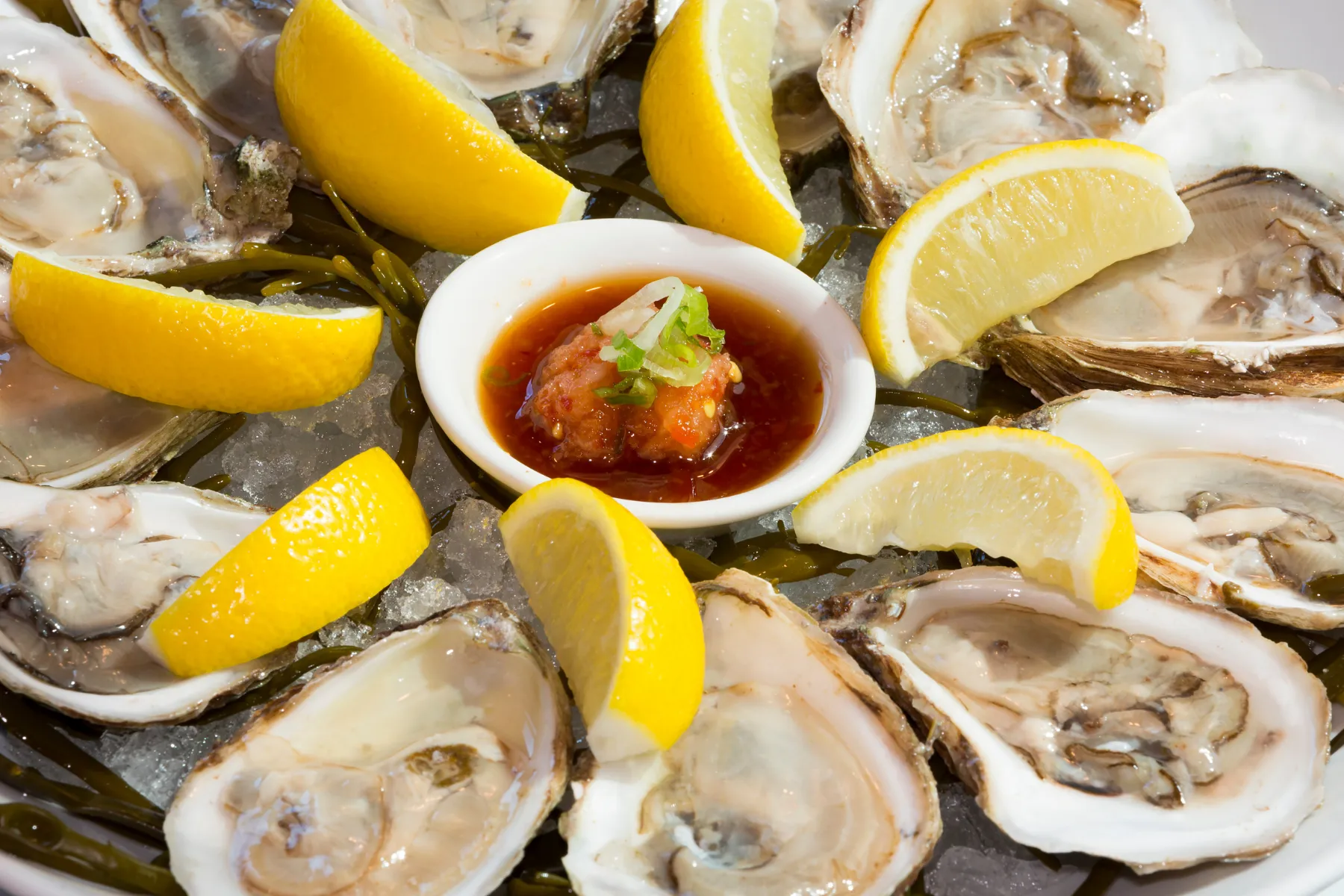 Freshly shucked oysters on ice served with lemon wedges and a small bowl of seafood sauce.